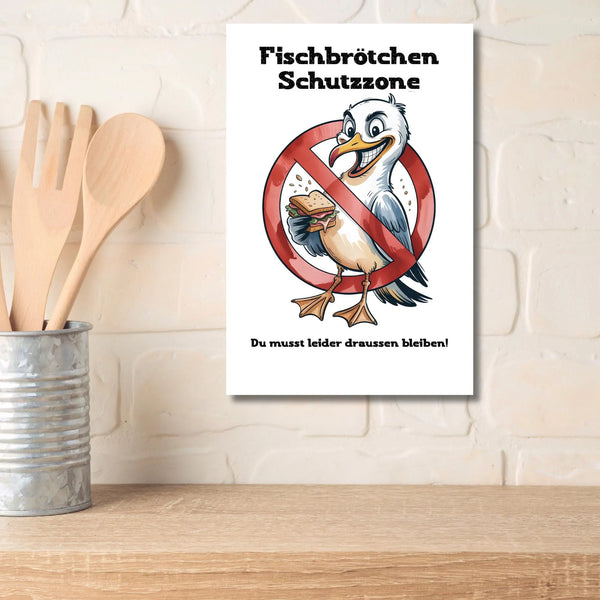 Weißes Poster mit einer Comic-Möwe, die ein Sandwich hält, durchgestrichen von einem roten Verbotsschild, Text: "Fischbrötchen Schutzzone - Du musst leider draussen bleiben", lustige maritime Deko.